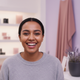 Close-up portrait of a smiling young woman with dark hair, looking directly at the viewer, against a softly blurred backgroun