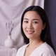 Close-up portrait of a radiant East Asian woman in her late 20s, smiling confidently, with a soft lavender and cream backgrou